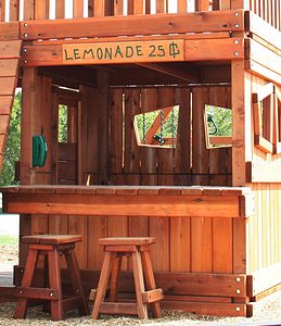 lemonade stand with counter, sign, and stools built into the lower cabin of this redwood swing set