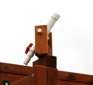 working white pvc water cannon has a redwood mounting swivel base, mounted to a redwood swing set, and has a redwood swivel base