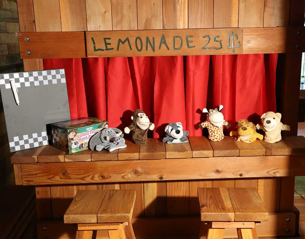 The Lemonade Stand attachment to a Backyard Fun Factory playset is turned into a puppet show stage by simply adding a red curtain.puppet theater, chalkboard, stage curtain, lemonade counter, animal puppets, swing set accessory, playset accessory, storytime