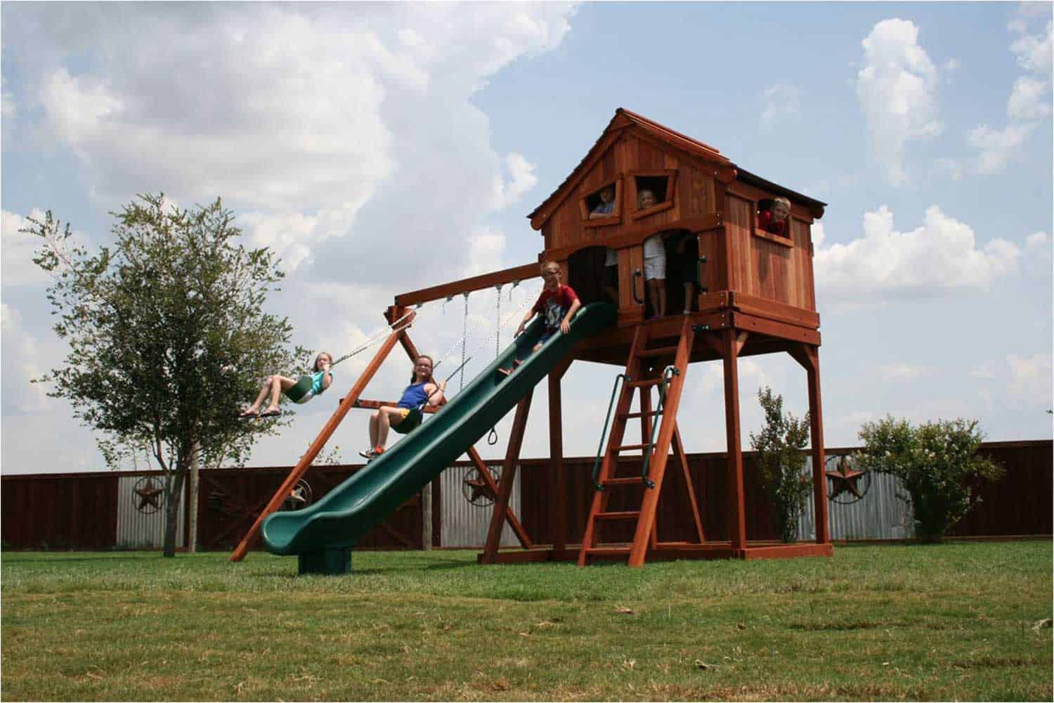 kids redwoood fort with swingset, upper cabin with crooked windows, slide, and deck ladder