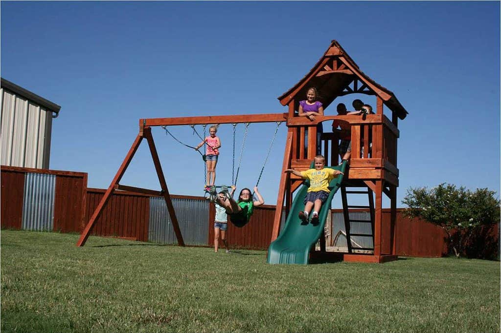 A beautiful redwood Fun Shack playset entertains several children who swing, slide and look around the Fun Shack covered deck. fun shack swing set with 3 swing positions, slide, swings