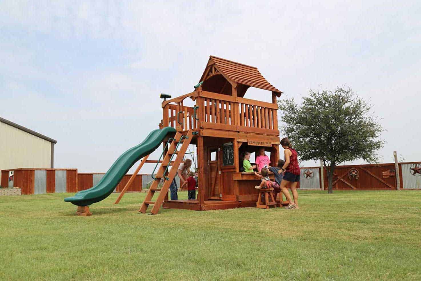 Trophy Club, Texas, maverick swing set with lower cabin and kids playing at the lemonade counter, and swinging on the swings