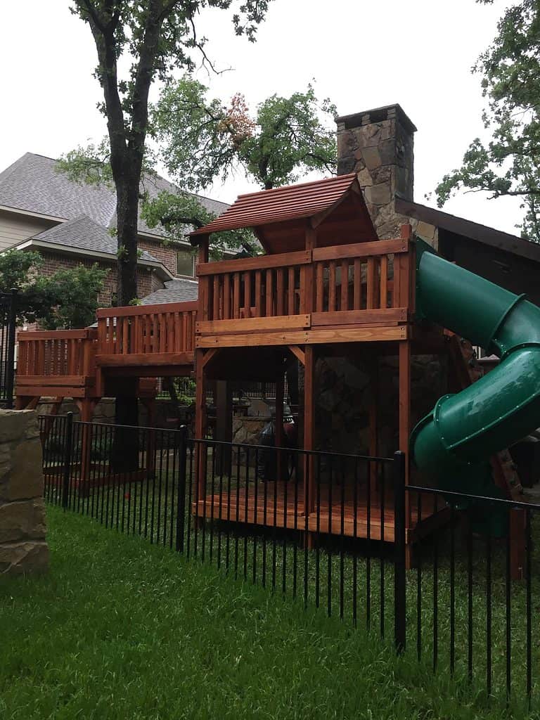 backyard playsets can be customized for your unique space like this multi-level playset that has limited space between the fence and the patio