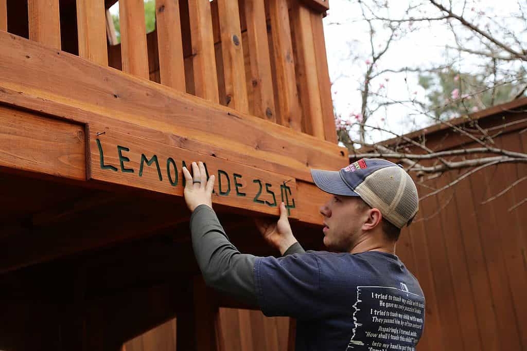 we install playsets all over the U.S., installer hanging lemonade sign on custom redwood swing set