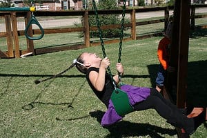 swing accessory, girl swinging and laughing as she spins around in circles in a green belt swing on a redwood backyard swing set