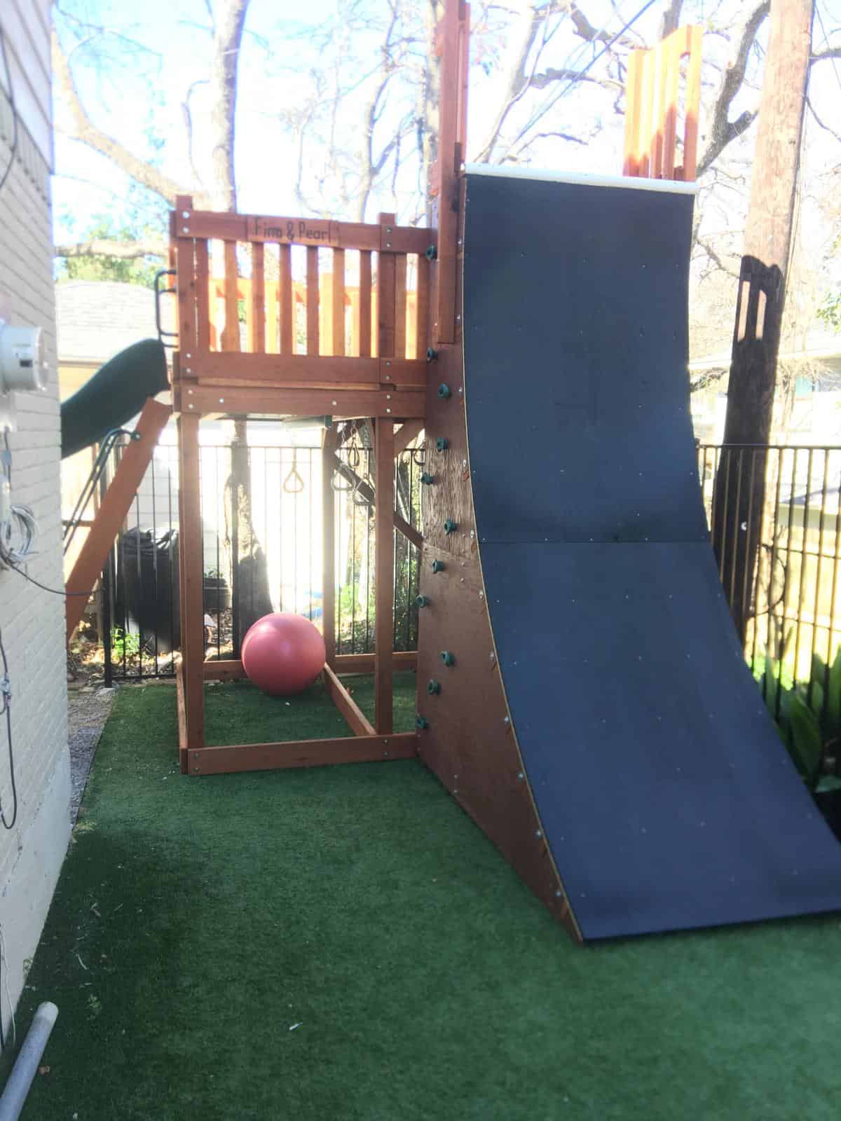 unique playset space in corner of yard with slide and rock wall in one direction and warp wall in different direction - small spaces