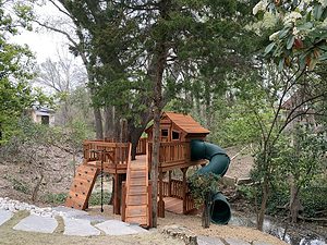 unique playset spaces, kids tree deck with fort, rock wall, spiral slide on side of creek