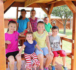Group of kids, experiencing child social development. sitting on the built in picnic table of a backyard redwood playset, and enjoying backyard playset benefits.