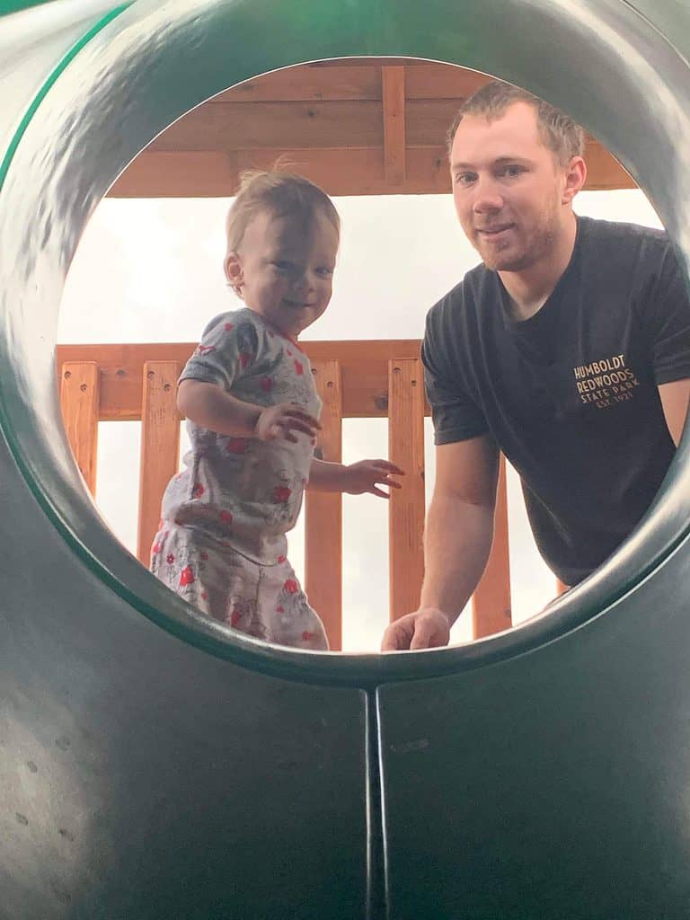 dad helping son go down the tube slide on the backyard playset