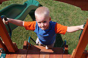 young boy climbing deck ladder on backyard playset