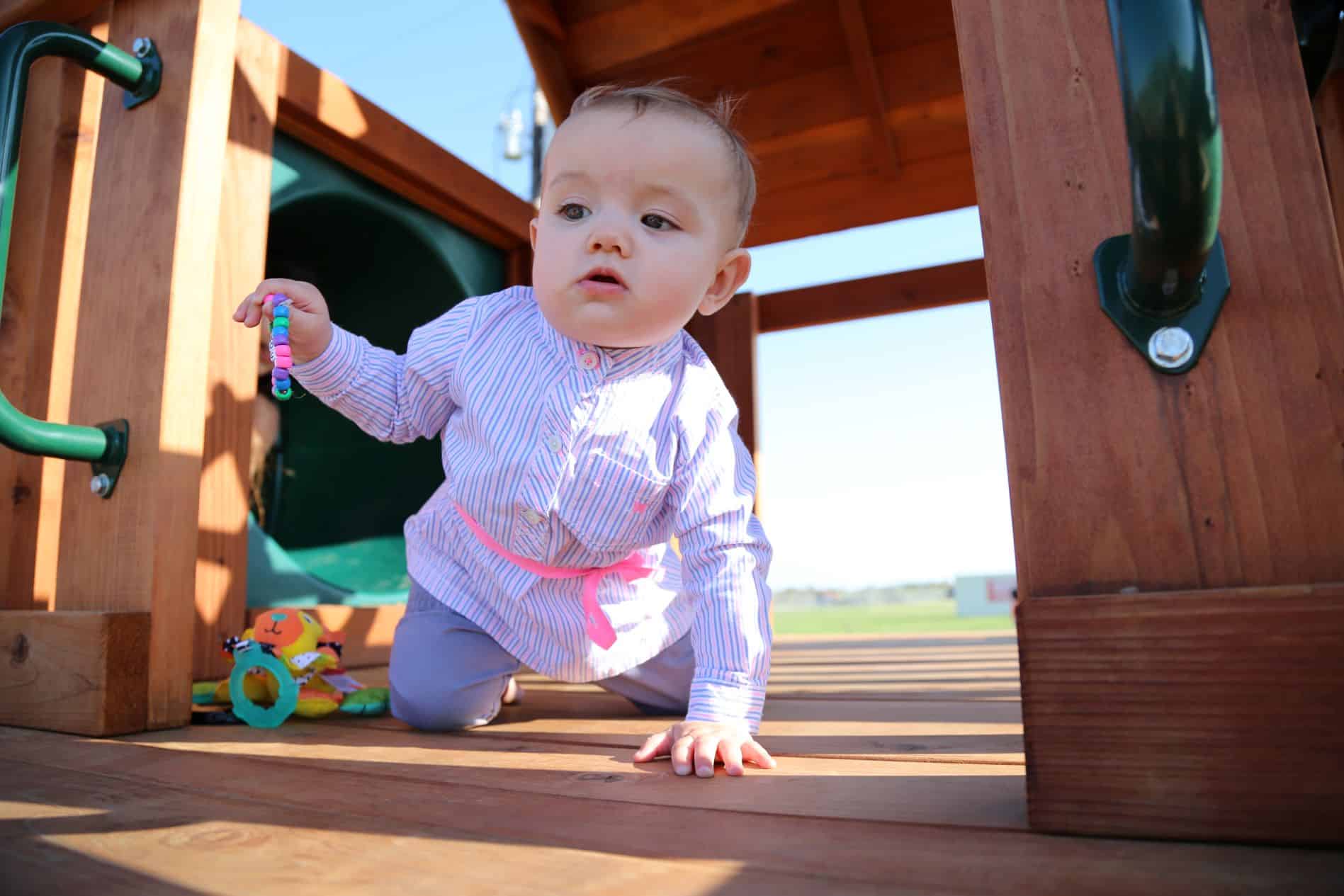 Hudson Oaks, Texas baby on redwood playset with slide behind her and grab handles in front of her