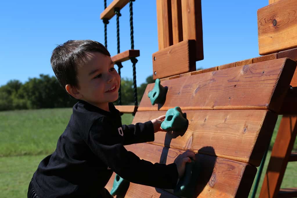 grandview, texas, little boy climbing rock wall on backyard fun factory swing set