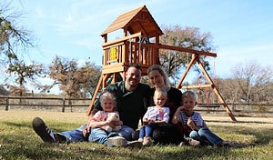 family sitting in backyard with playset in background