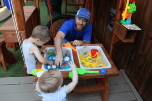 dad with son and daughter playing with sensory table in backyard playset