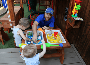 dad with son and daughter playing with sensory table in backyard playset