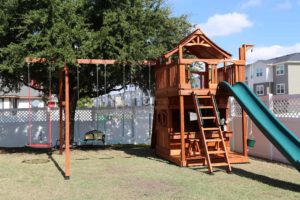 Fort stockton playset in residential backyard with swings, slide and lower cabin.