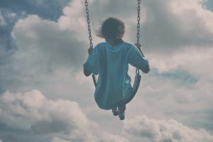 Child swinging surrounded by clouds