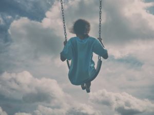 child swinging on her playset trying to reach the clouds in the sky