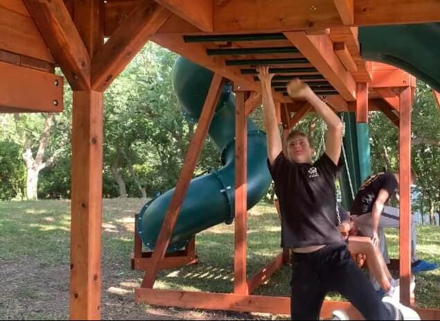 Young man with a goal to reach the end of the monkey bars, on his Backyard Fun Factory Playset.