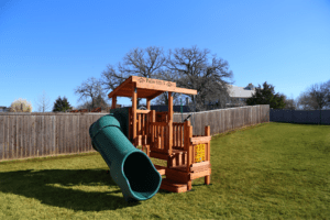 Backyard Fun Factory Toddler Trainer playset in Texas, featuring a clubhouse, tube slide, tic-tac-toe panel, toddler swing, and lower play area. Designed for young children to safely climb, slide, and develop confidence through active outdoor play.