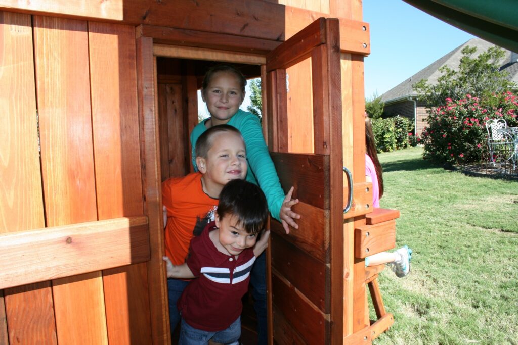 Family of 3 children looking out a Backyard Fun Factory fort door.