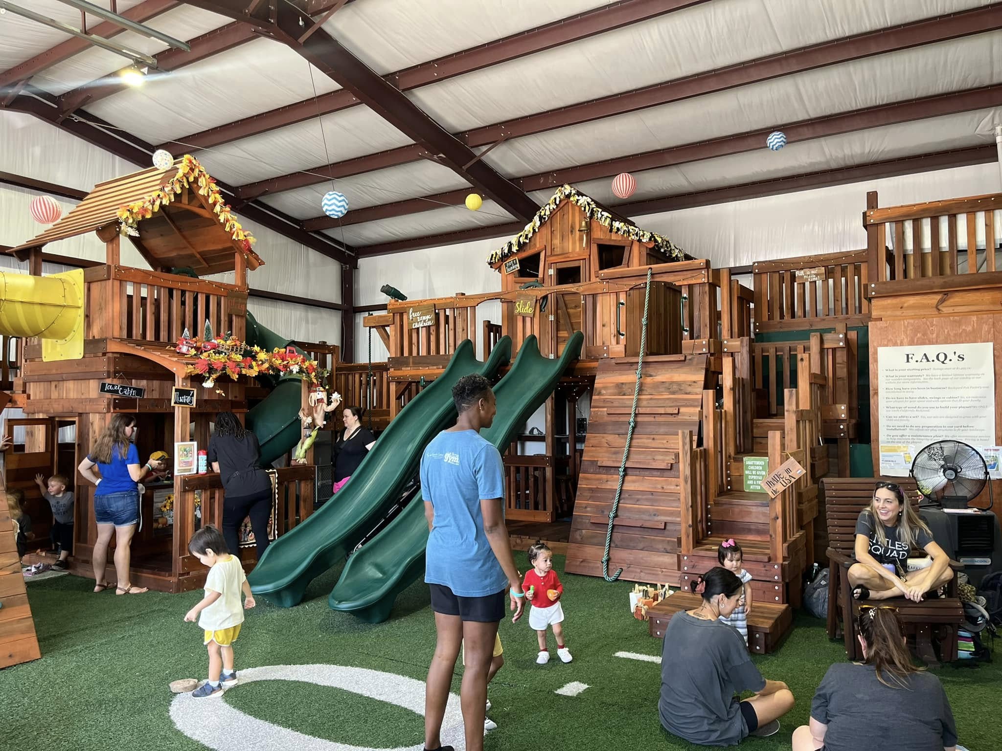 Families and children exploring premium redwood playsets and swing sets inside Backyard Fun Factory’s Fort Worth Swing Set Showroom. The interactive indoor space features slides, climbing walls, and playhouses, allowing customers to experience the quality and craftsmanship firsthand.