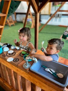 Young boy and girl playing with a wooden mud kitchen at Backyard Fun Factory Frisco Swing Set Showroom, exploring interactive features of custom redwood playsets for kids.