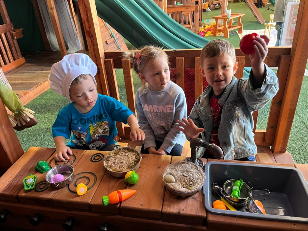 Young children playing with a wooden mud kitchen inside Backyard Fun Factory’s Fort Worth Swing Set Showroom, enjoying the fun.