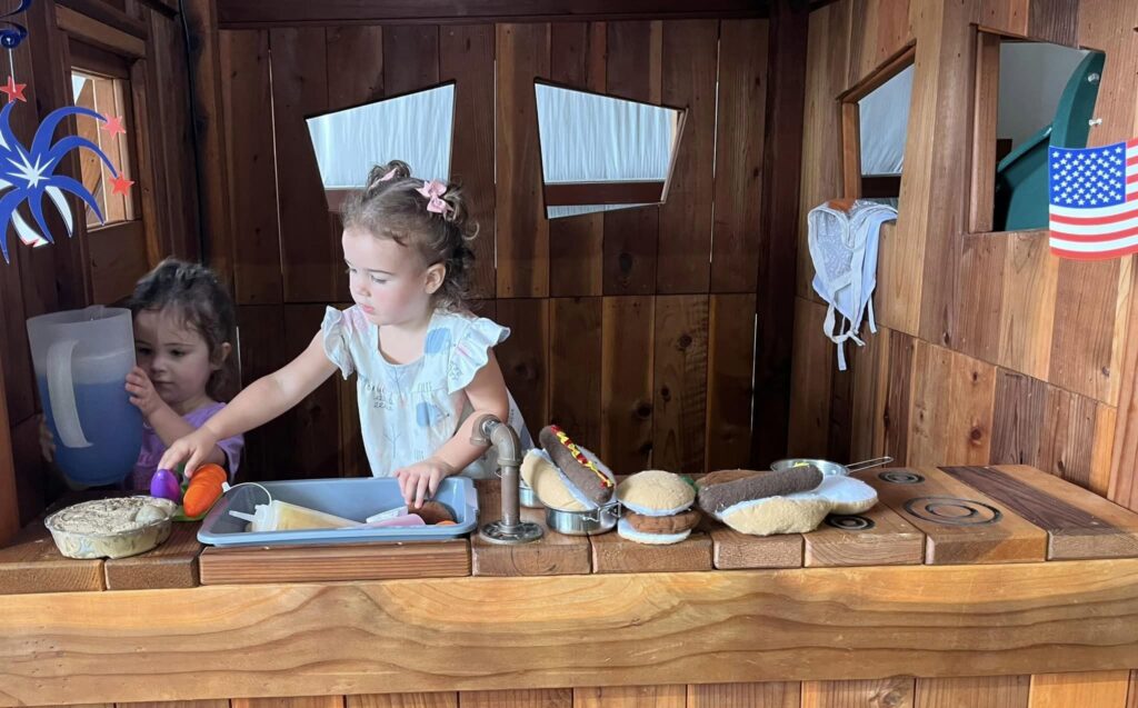 Two adorable little girls, busy playing in a Backyard Fun Factory Mud Pie Kitchen.