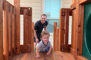 Father watching his son playing on a Backyard Fun Factory playset.