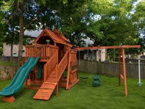 A Backyard Fun Factory backyard playset, created to be safe for children to enjoy. Custom California redwood swing set installed in Carrollton, Texas featuring an elevated fort, covered playhouse, rock wall, slide, swing beam, climbing ramp, picnic table, and toddler play area. Backyard Fun Factory designs and installs custom wooden playsets for families throughout Carrollton, Dallas County, and North Texas.