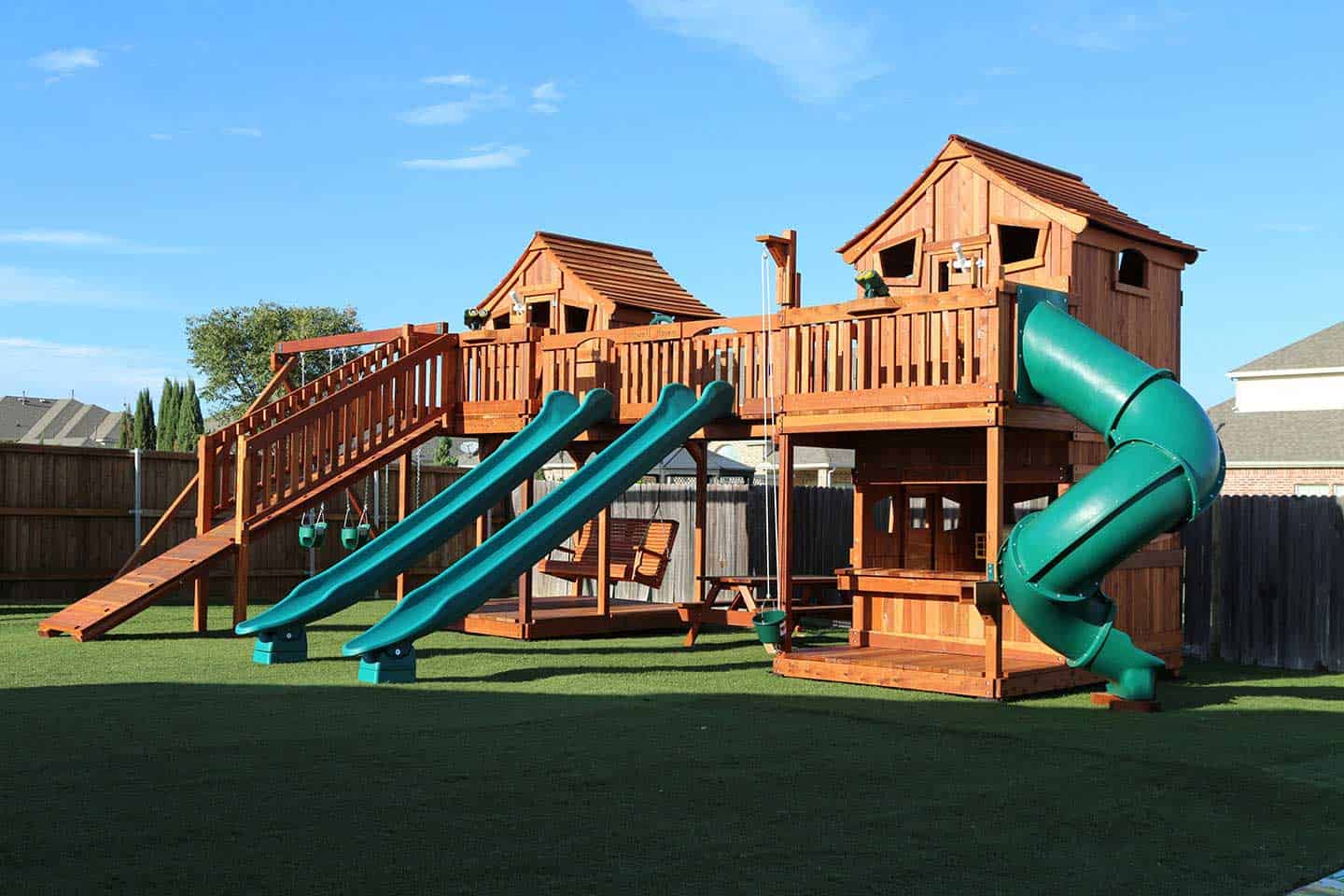 Bridged redwood playset with swings and adult porch swing. Spiral slide and rocket slides accessorize this fun backyard swing set.